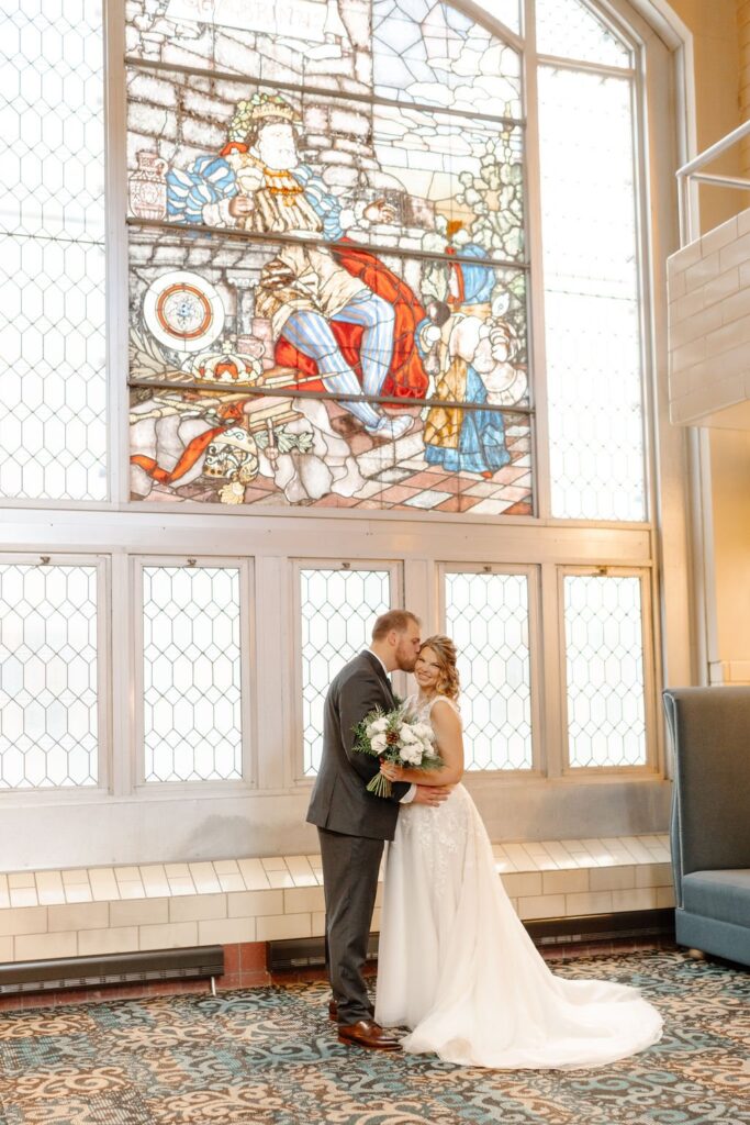 bride and groom kissing in front of a stained glass mural at wedding venues milwaukee wi