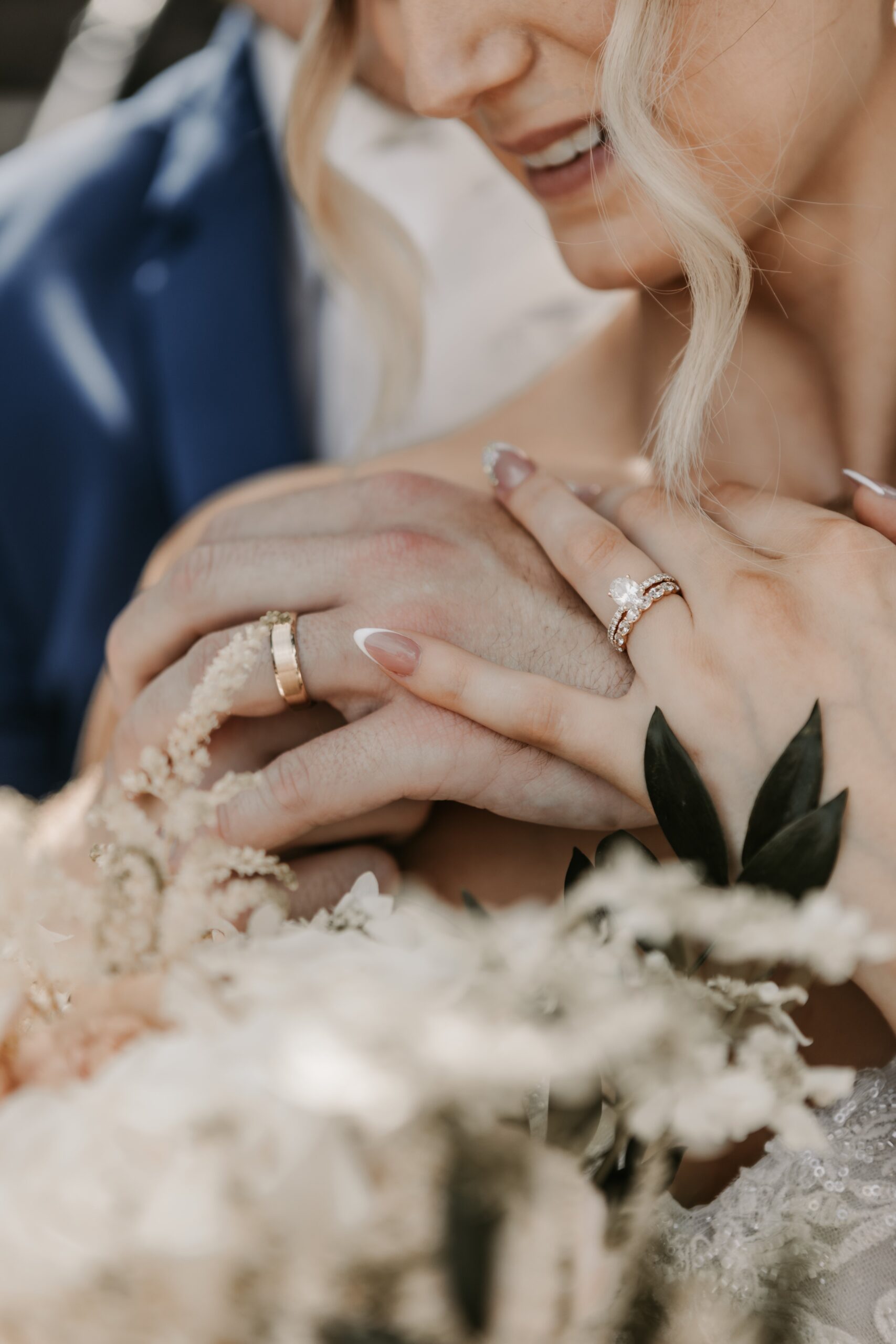 close up image by dream weddings in milwaukee wisconsin of bride and groom on wedding day holding hands and showing rings with floral bouquet in foreground