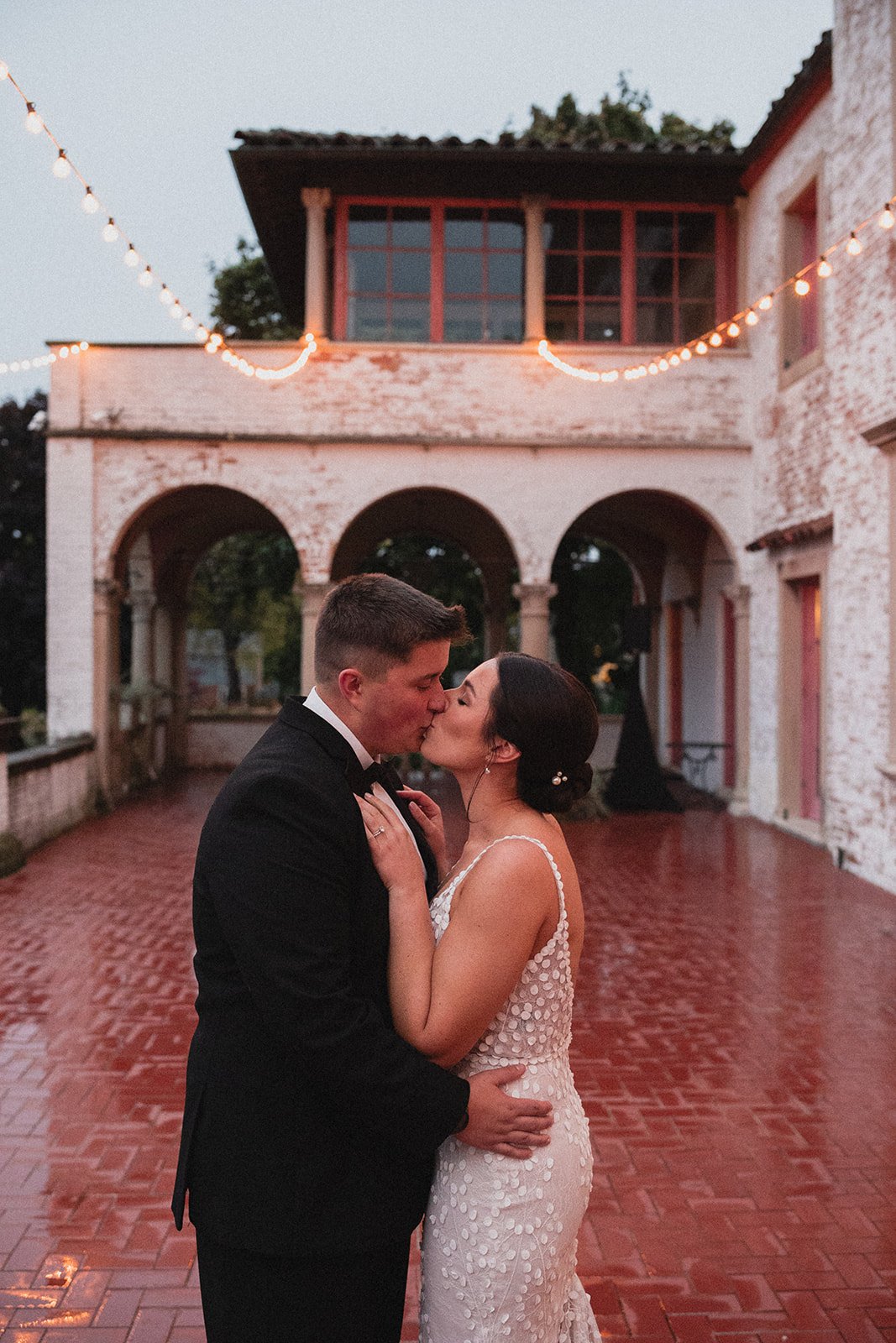 the bride and groom stealing a kiss under the lights during their rainy outdoor wedding
