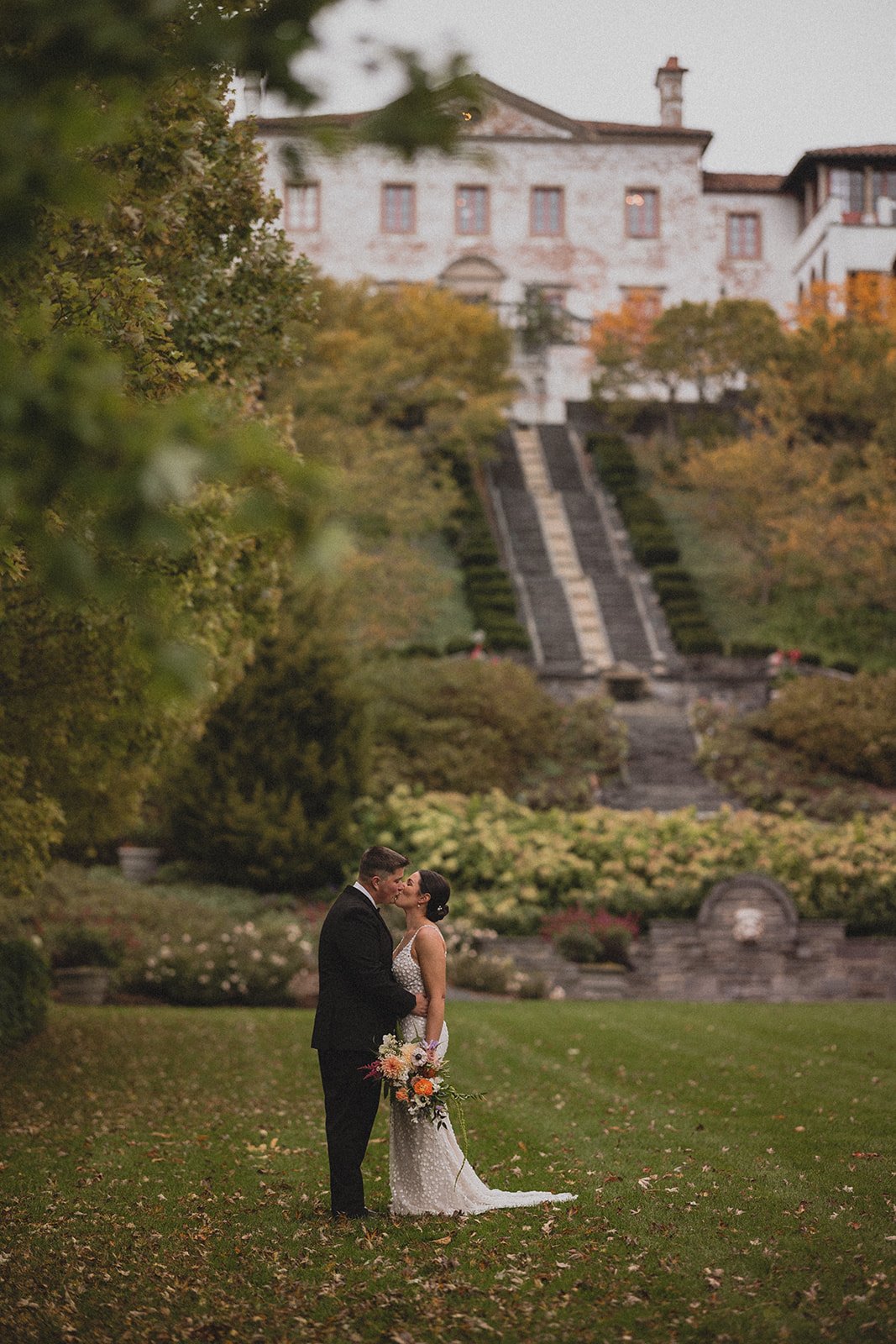 a full portrait shot of a bride and groom kissing in the lawn of their outdoor wedding venue