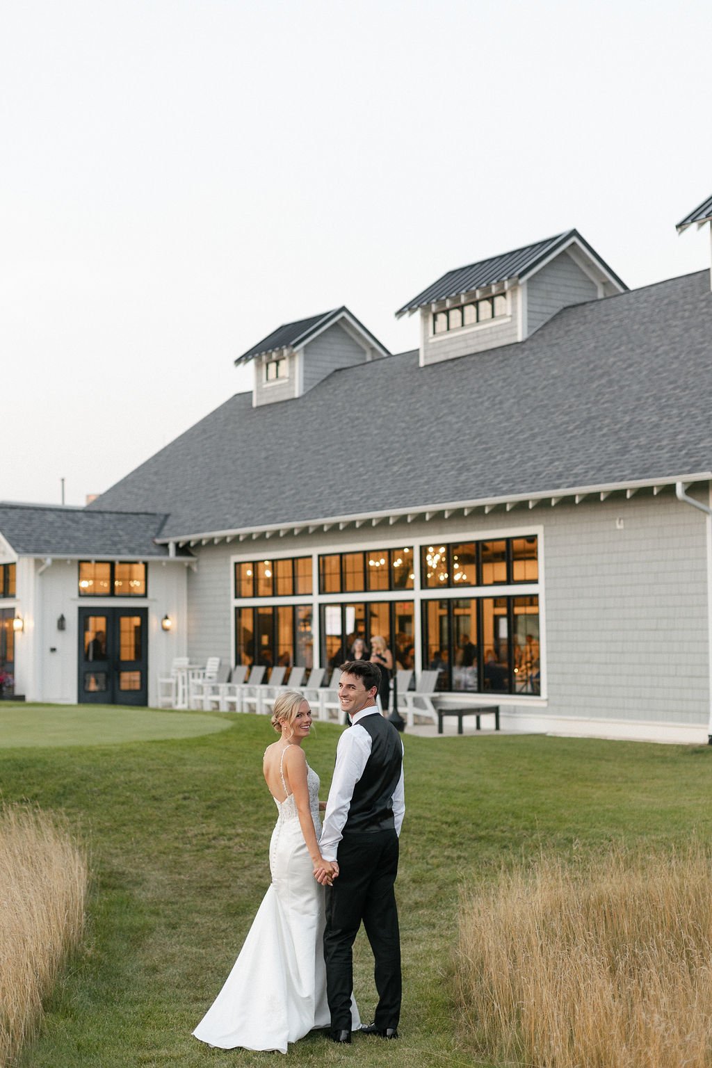 The bride and groom stealing a peak at the photographer and wedding event planner at an outdoor wedding venue near milwaukee wi
