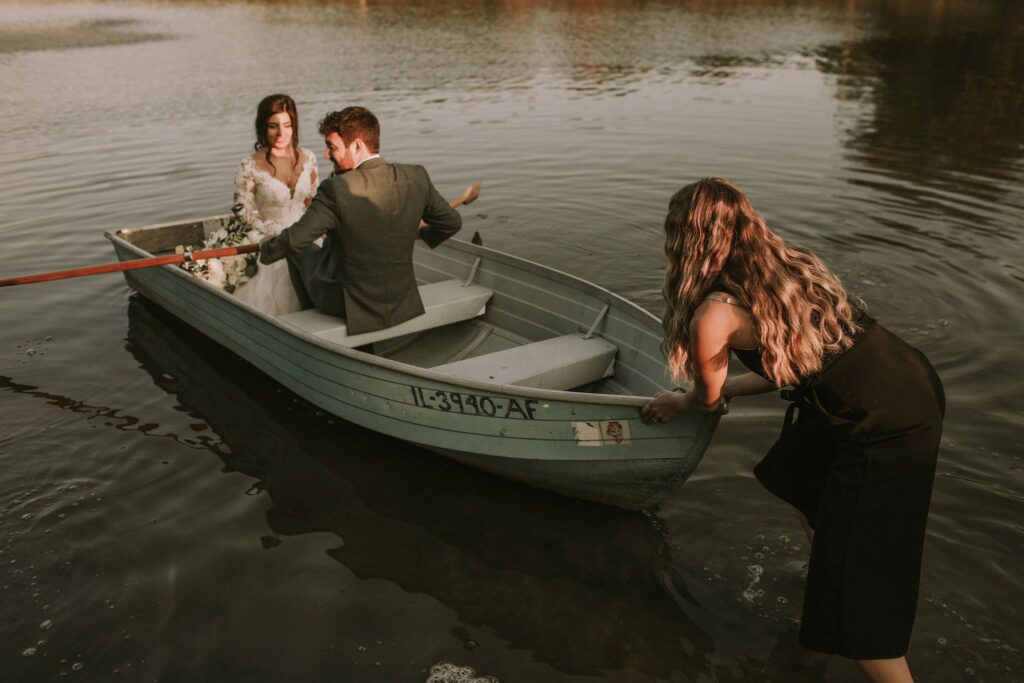 liz from dream weddings wi pushing a row boat onto the water for the perfect bride and groom portrait photos at a lake geneva wedding