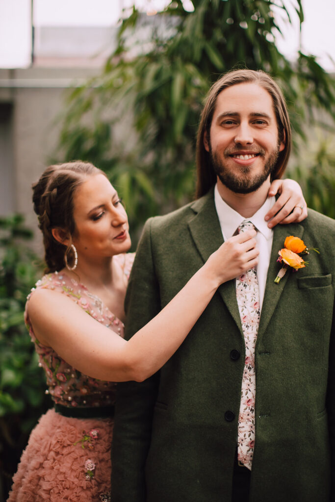 Bride smiling while straightening the groom’s tie and boutonniere during a quiet moment at one of the most romantic wedding venues in Madison