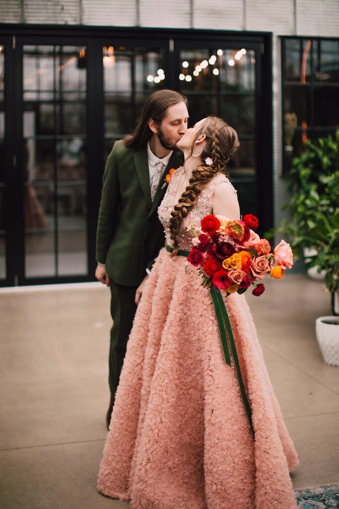 Bride holding a vibrant bouquet of roses while sharing a kiss with the groom inside an industrial wedding venue in Madison WI