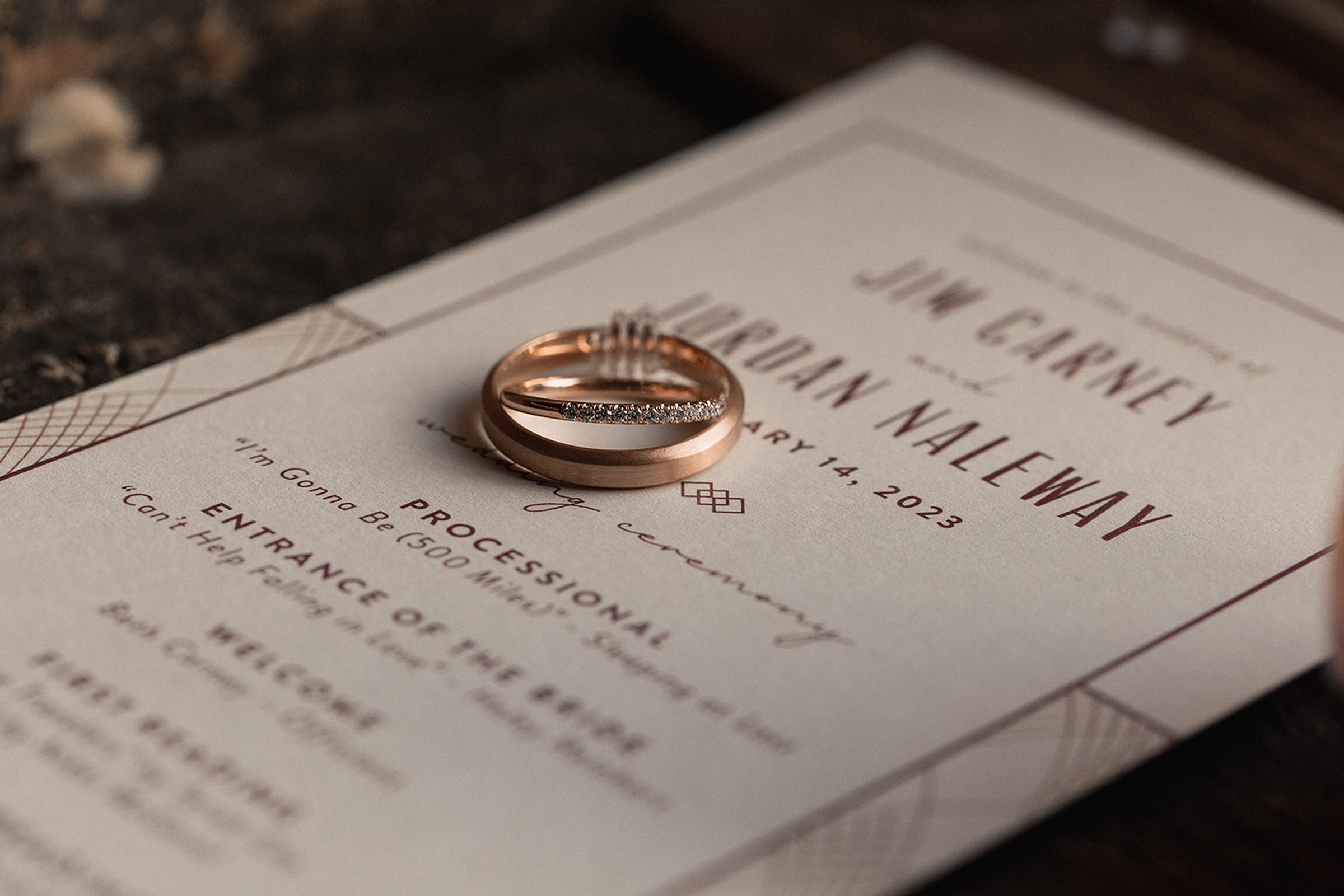 Close-up of rose gold wedding bands resting on a printed wedding invitation, highlighting elegant stationery details from a Madison WI wedding venue celebration