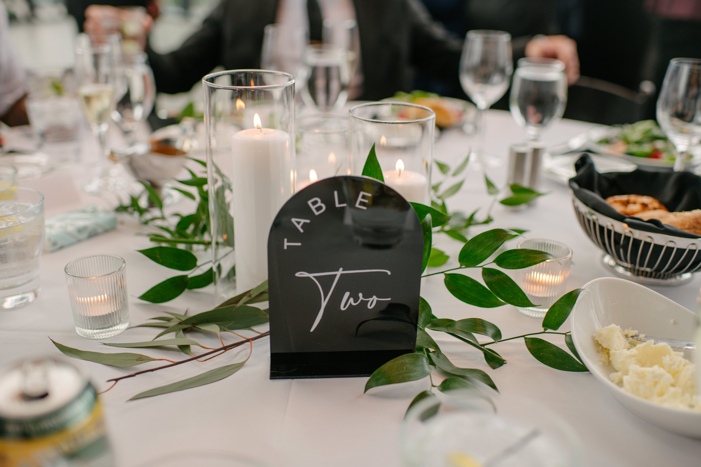 Modern table number sign surrounded by greenery, candles, and elegant place settings at a wedding reception venue in Madison WI