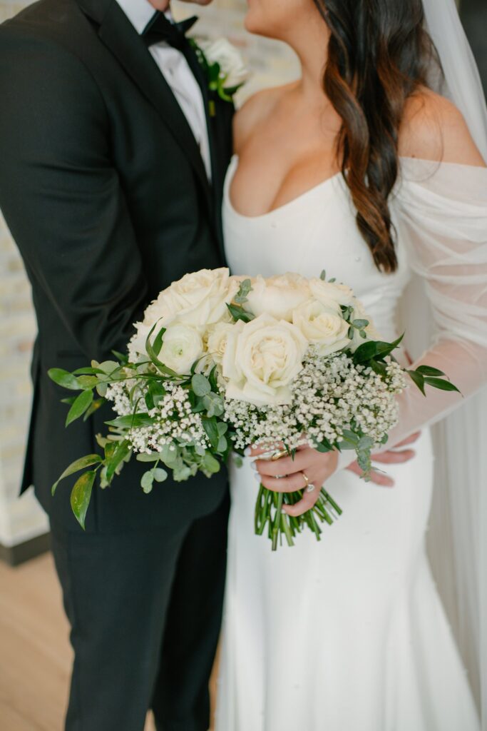 Bride holding a white rose bouquet as she stands close with the groom during a romantic portrait at a Madison WI wedding venue