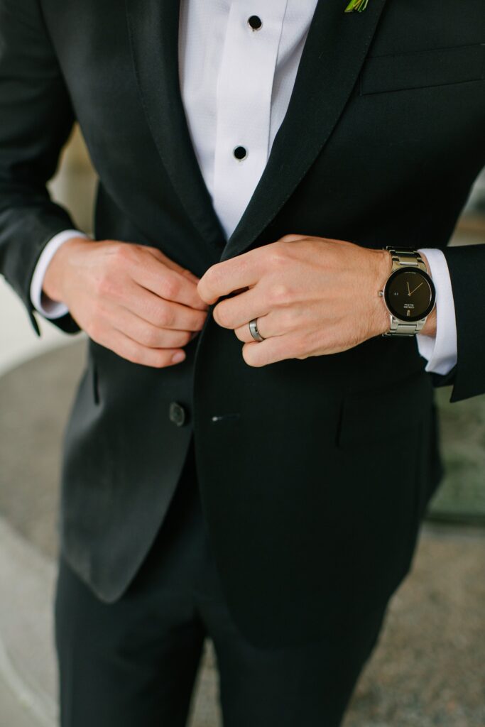 Groom buttoning his black tuxedo jacket during wedding preparations at one of the most elegant wedding venues Madison WI has to offer