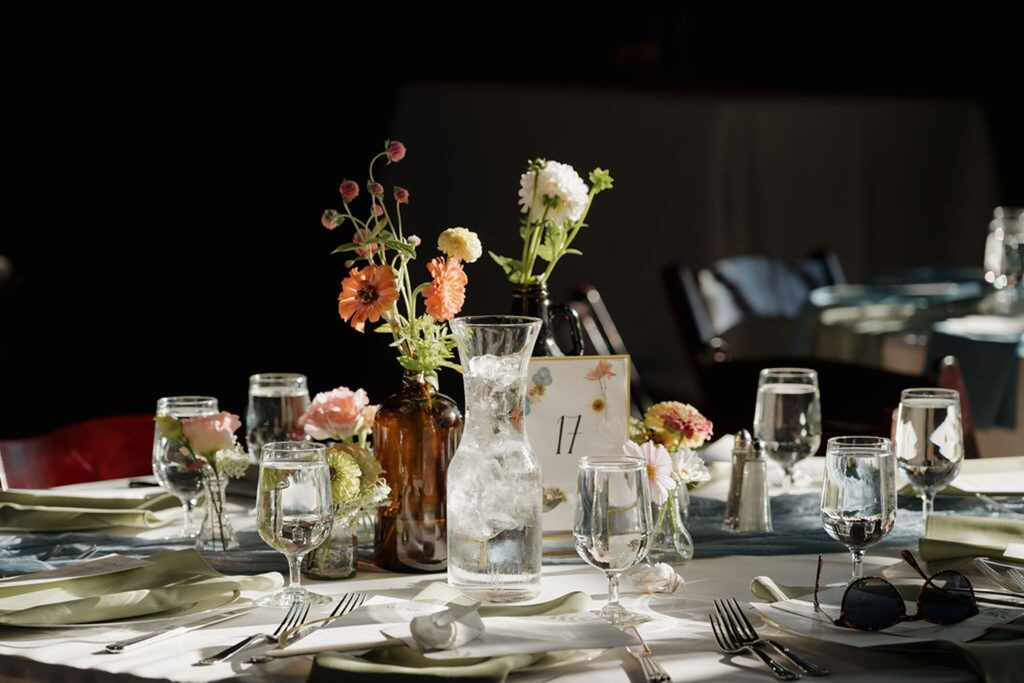 Sunlit reception table with floral centerpieces, table number, and elegant place settings at one of the most charming wedding venues in Madison