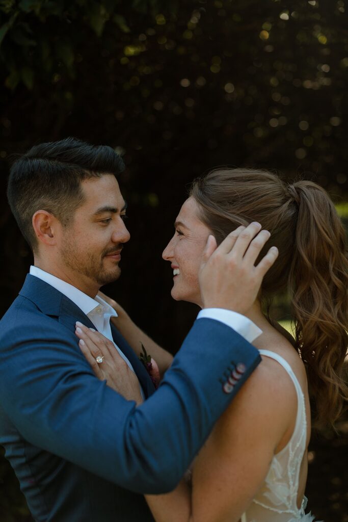 Couple shares an intimate moment during their wedding portraits, smiling at each other outdoors