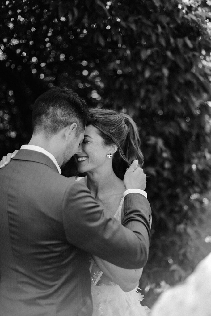 Black and white wedding portrait of a couple touching foreheads and laughing together outside