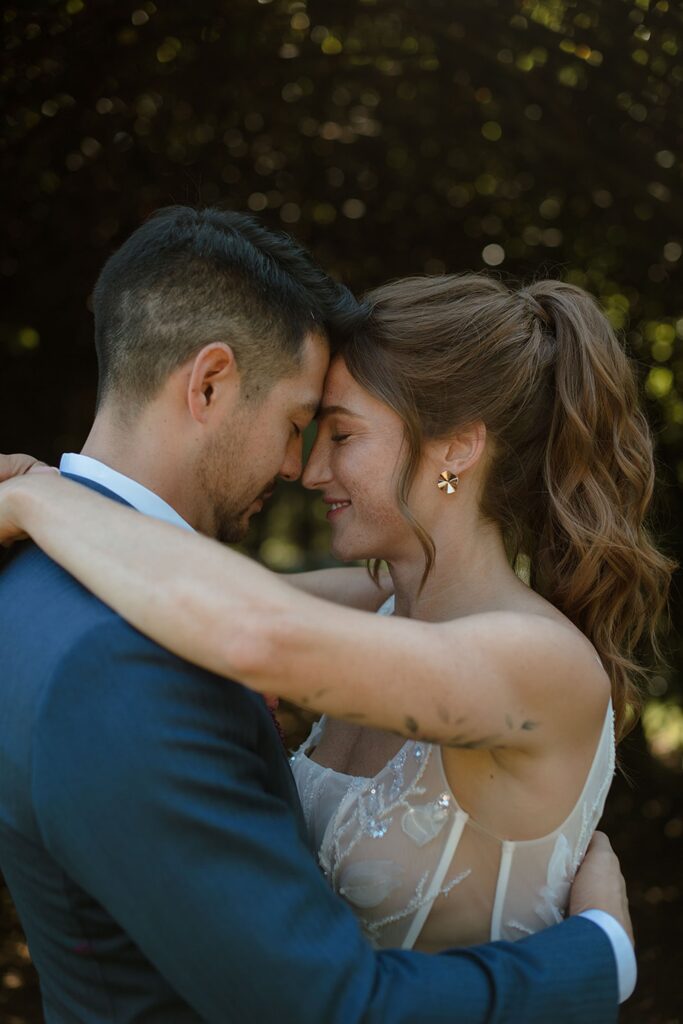 Bride and groom embrace during outdoor wedding portraits, eyes closed and smiling