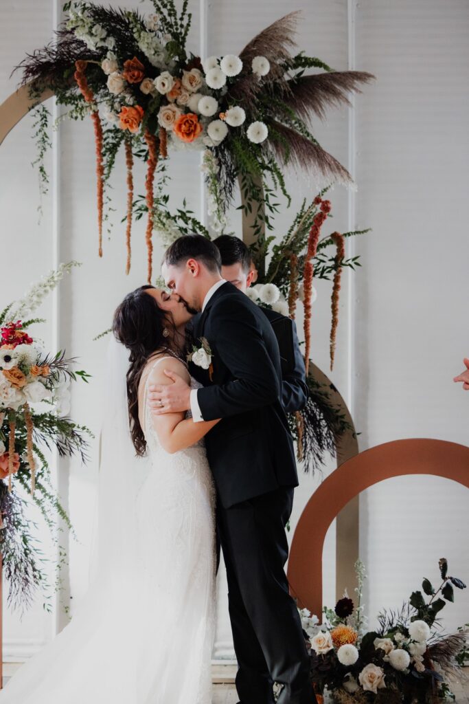 Bride and groom sharing their first kiss beneath a floral ceremony arch at a wedding venue in Madison WI