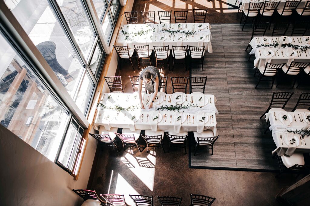 Wedding planner carefully arranging place settings and greenery at a wedding venue in Madison WI before guests arrive