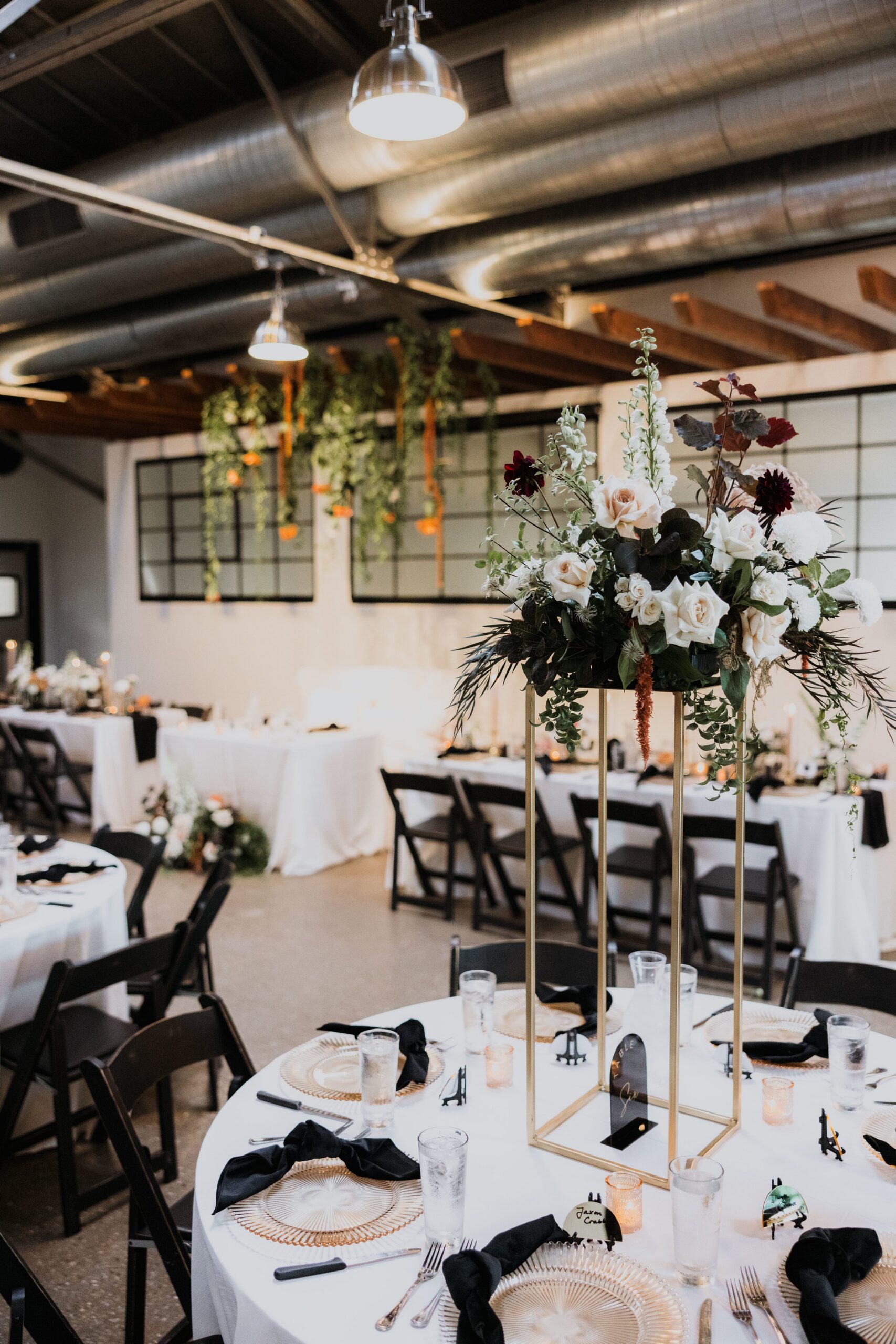 Industrial-style wedding reception space with long tables, tall floral centerpieces, and hanging greenery, showcasing elegant indoor weddings Madison WI and unique places to get married in Madison WI.