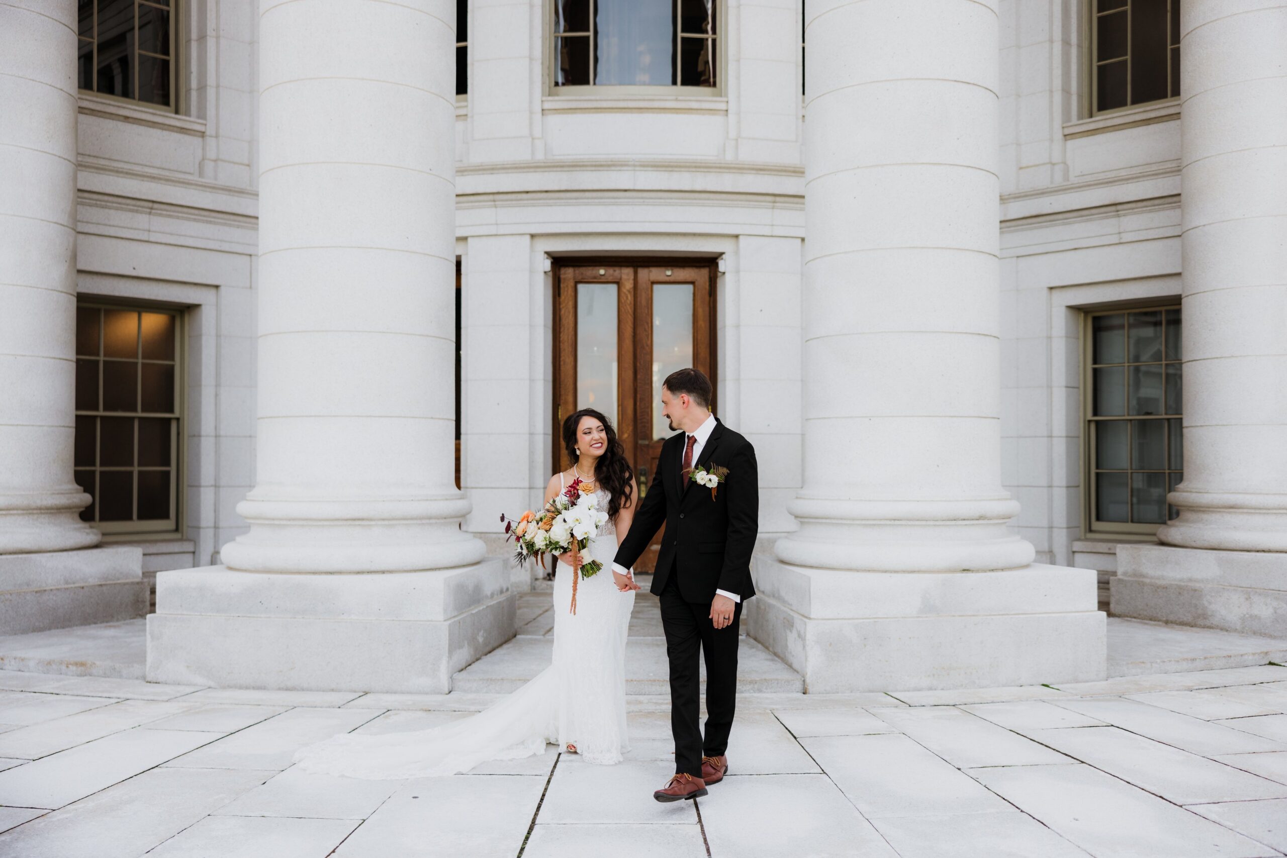 Bride and groom standing together in front of the grand columns of the Wisconsin State Capitol, capturing a timeless portrait from weddings Madison WI and a popular place for getting married in Madison WI.