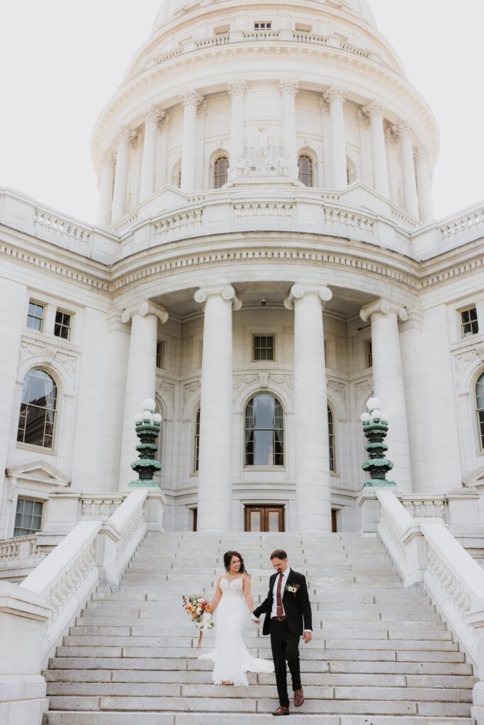 Bride and groom posing on the grand steps of the Wisconsin State Capitol, showcasing an iconic backdrop for weddings Madison WI and a memorable place for getting married in Madison WI.