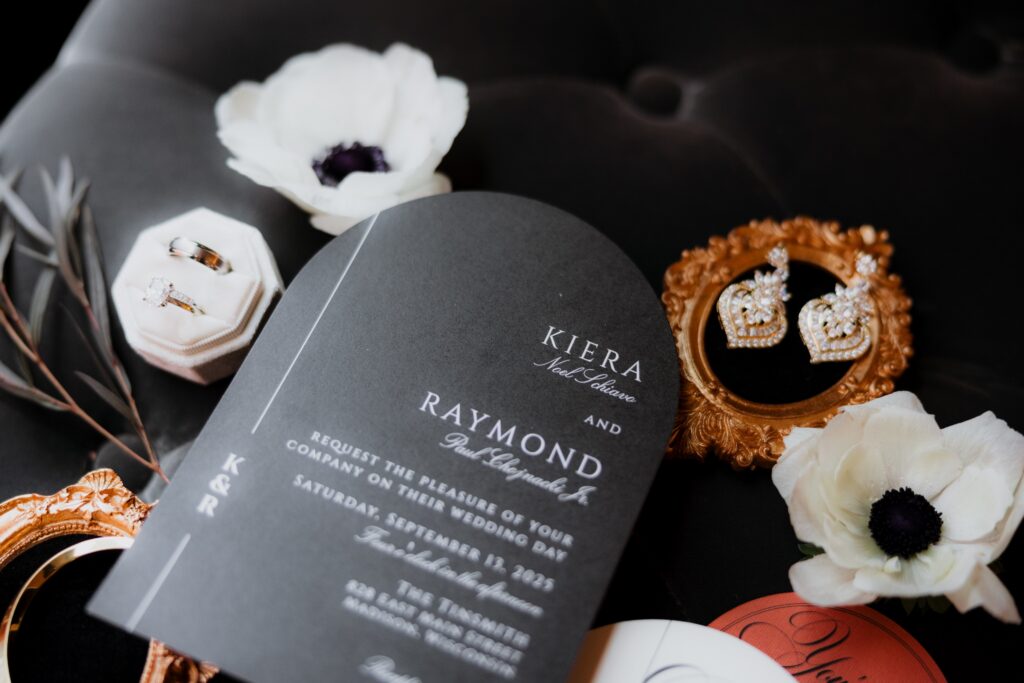 Elegant wedding invitation suite with rings, earrings, and floral details arranged on a dark background, showcasing stylish details from weddings Madison WI and inspiration for getting married in Madison WI.