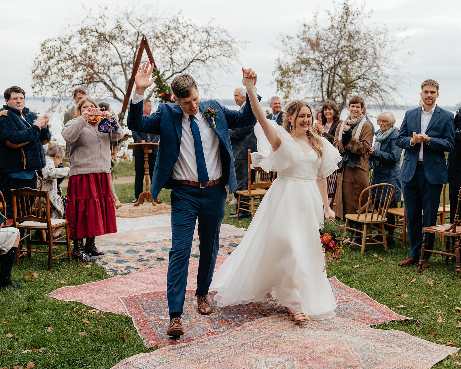 Bride and groom celebrating at the end of their outdoor ceremony as guests cheer, capturing the joy of getting married in Madison WI at a scenic lakeside wedding venue.