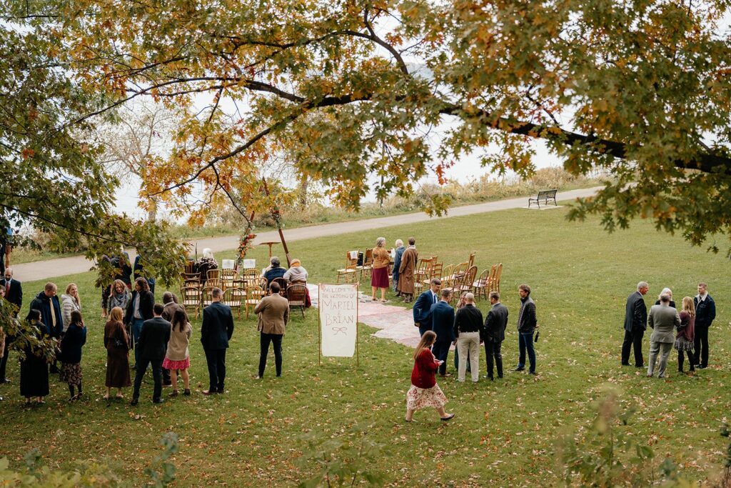 Outdoor wedding ceremony with guests seated on a lawn as a couple exchanges vows under a wooden arch, showcasing a scenic example of weddings Madison WI and popular places to get married in Madison WI.