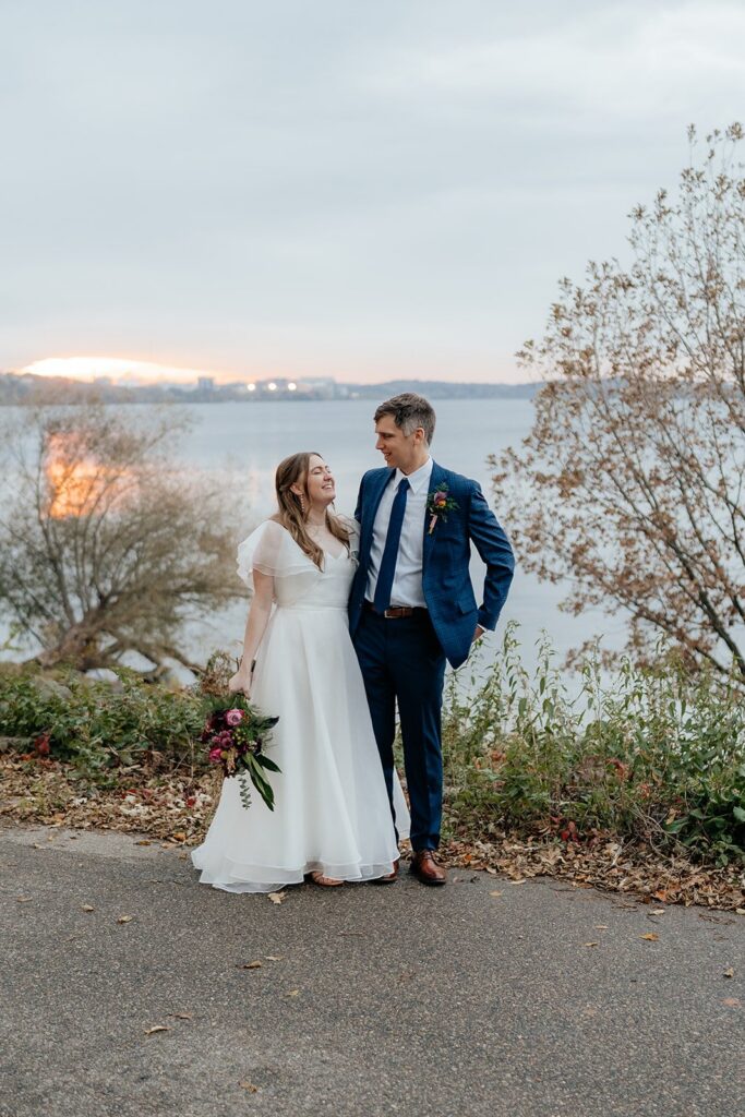 Bride and groom standing together along a lakeside path at sunset, capturing a romantic moment from weddings Madison WI and scenic places to get married in Madison WI.