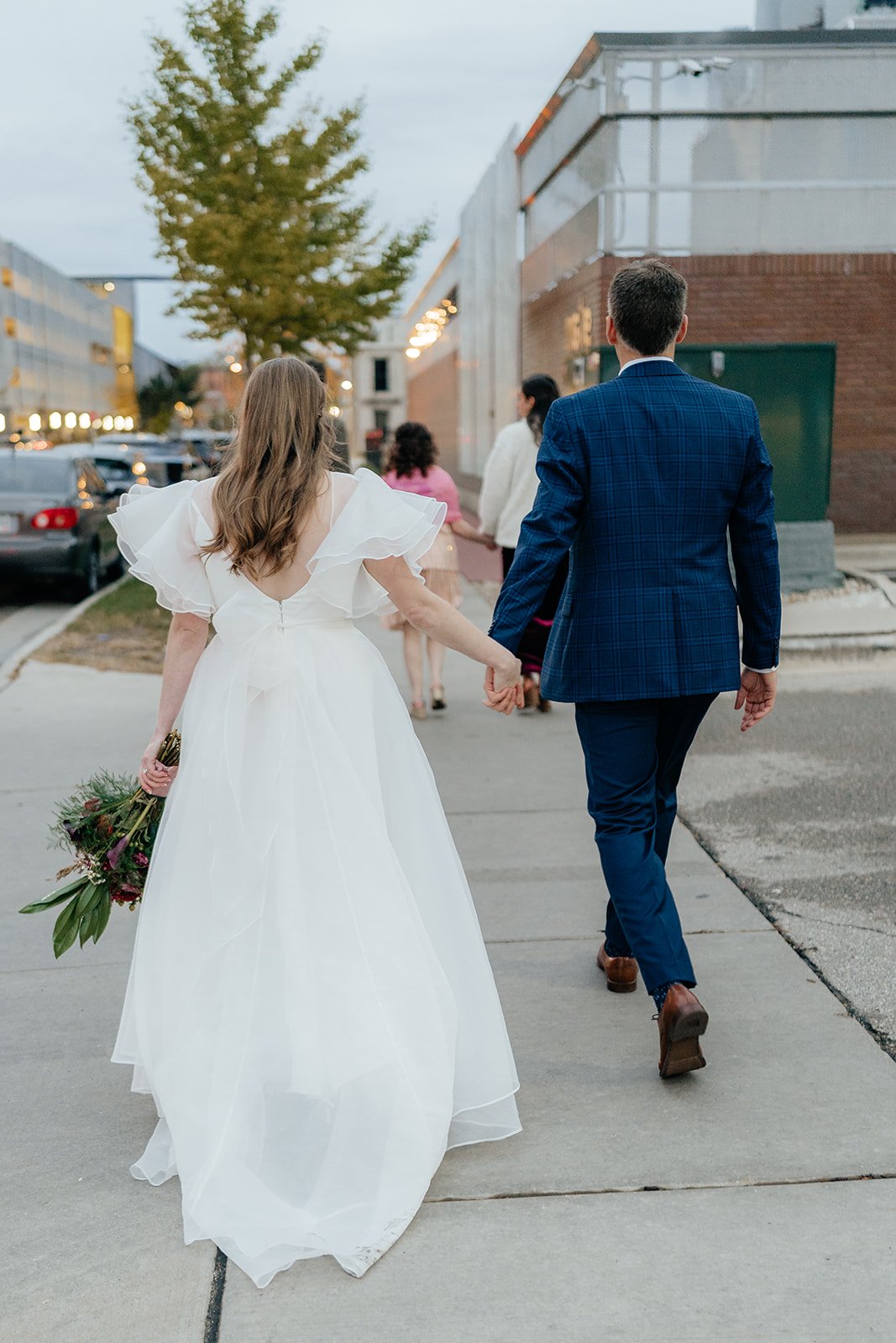 Bride and groom holding hands while walking through downtown after their ceremony, capturing a candid moment from getting married in Madison WI and modern weddings Madison WI.