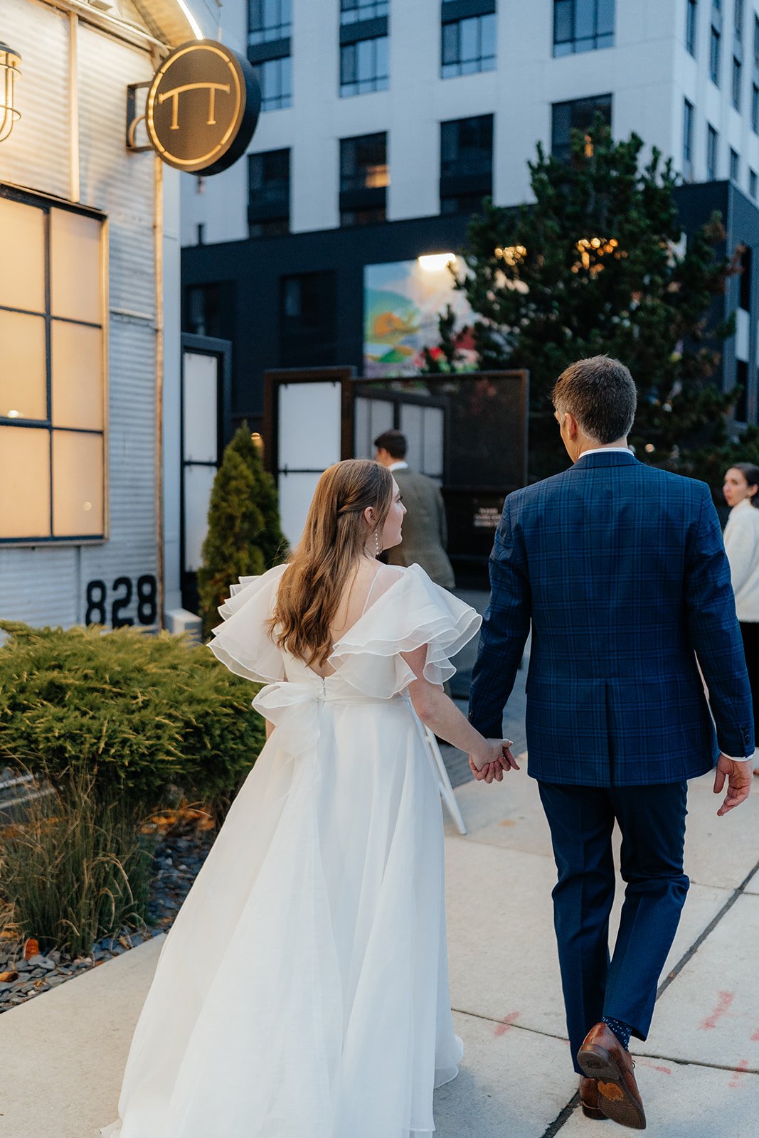 Bride and groom holding hands while walking toward a modern Madison venue entrance, capturing a candid moment from getting married in Madison WI and stylish weddings Madison WI.
