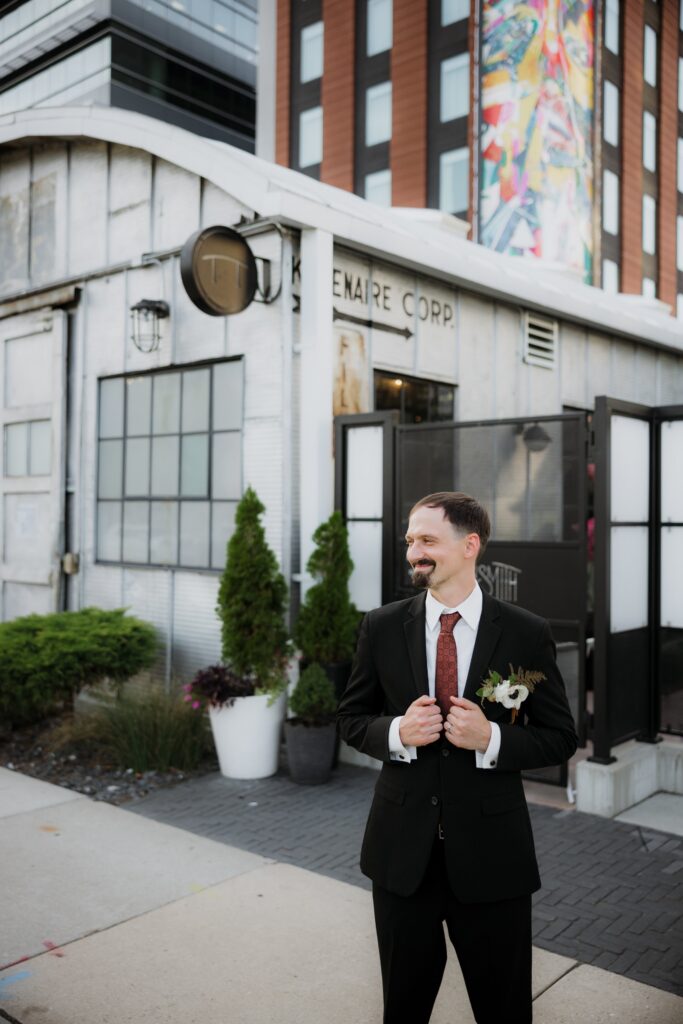 Groom in a black tuxedo standing outside a historic venue entrance, capturing a stylish moment from weddings Madison WI and unique places to get married in Madison WI.