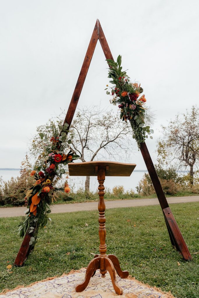 Rustic triangular wooden wedding arch with autumn floral arrangements and a small podium set for an outdoor ceremony, a charming setup for getting married in Madison WI and weddings Madison WI.