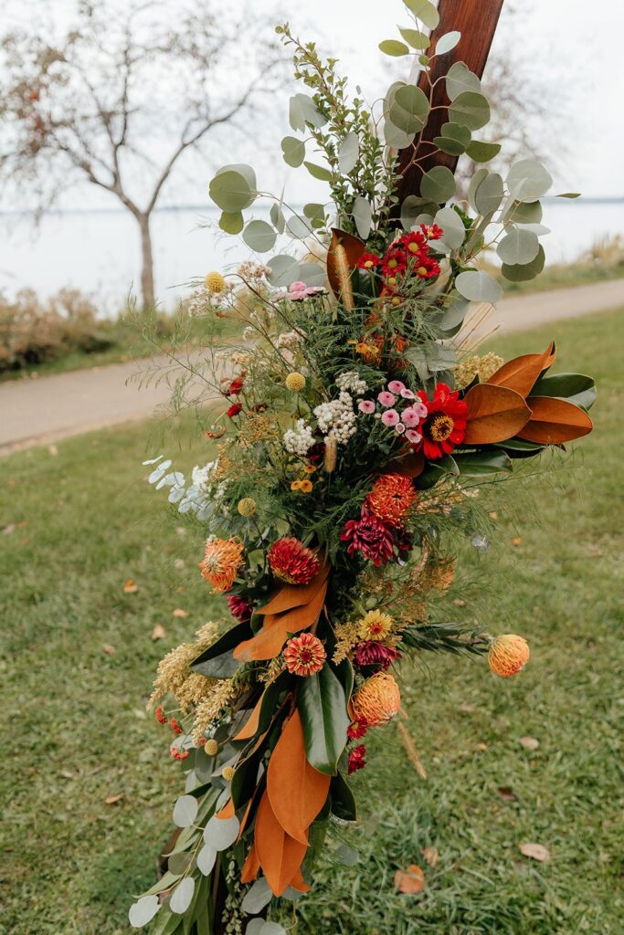 Autumn floral arrangement with greenery and orange blooms decorating a wooden wedding arch at an outdoor venue, a beautiful detail often seen at weddings Madison WI and places to get married in Madison WI.