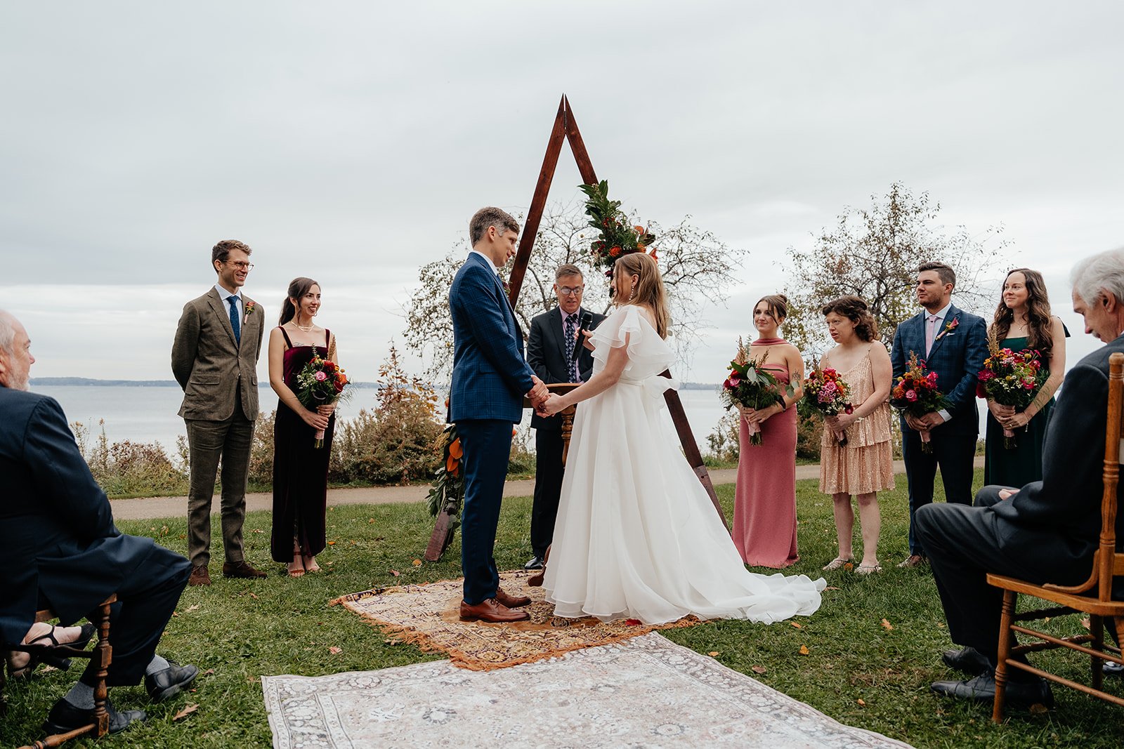 Couple exchanging vows during a lakeside outdoor ceremony with guests seated on the lawn, capturing the beauty of getting married in Madison WI and scenic places to get married in Madison WI.