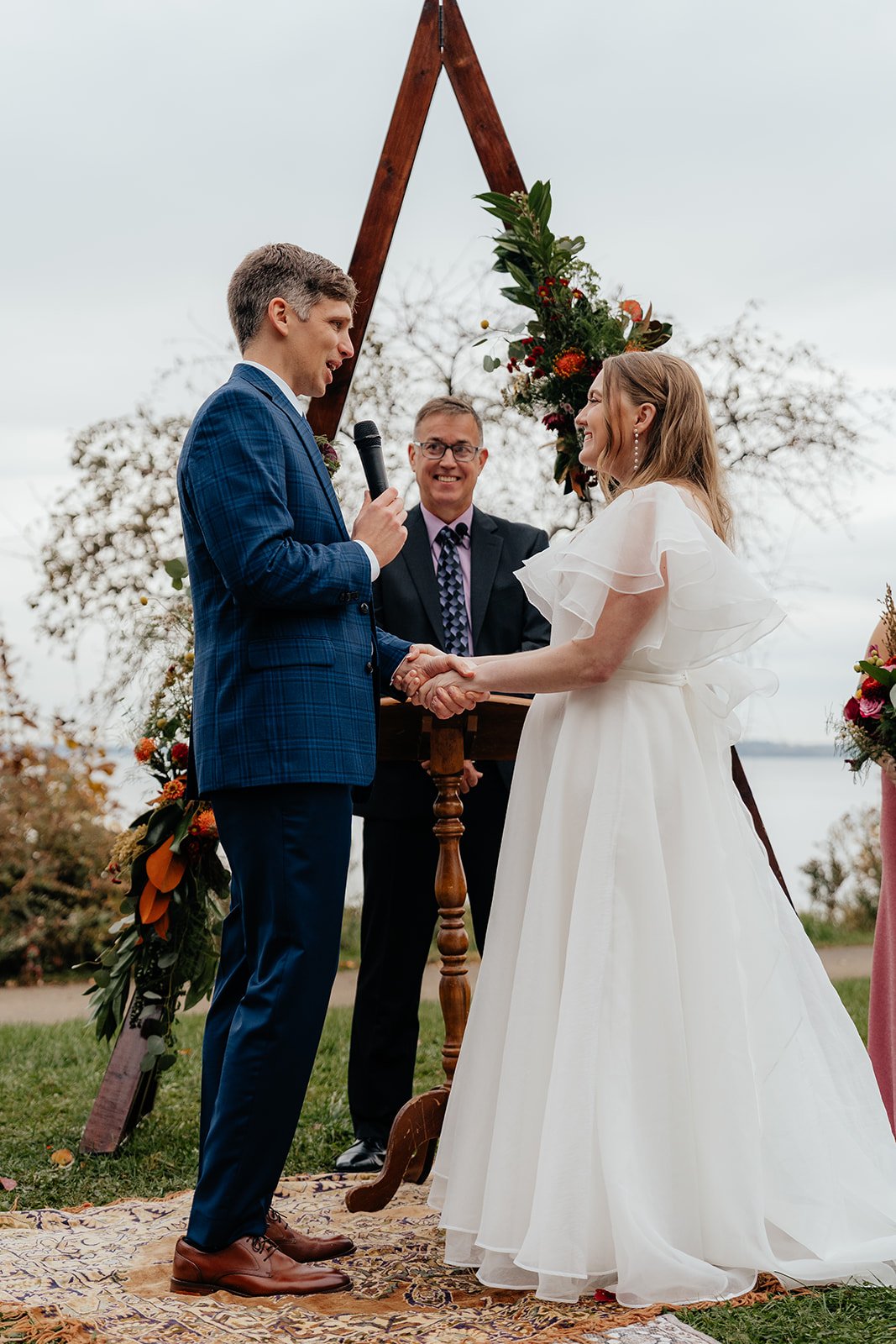 Couple exchanging vows during a lakeside outdoor ceremony beneath a wooden arch with floral arrangements, capturing the beauty of getting married in Madison WI and scenic weddings Madison WI.