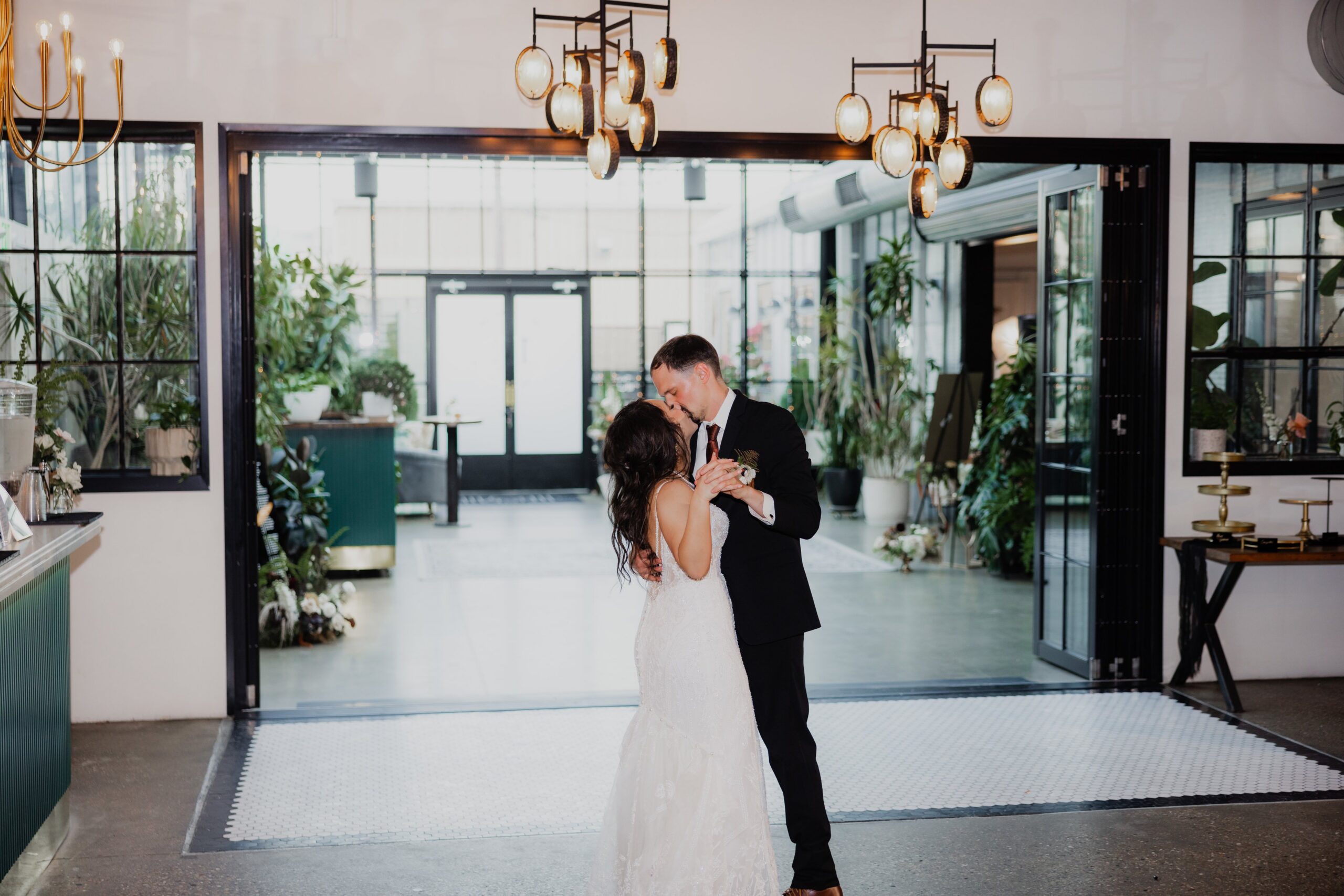 Bride and groom sharing their first dance inside a modern venue with greenery and large windows, capturing the elegance of indoor weddings Madison WI and stylish places to get married in Madison WI.